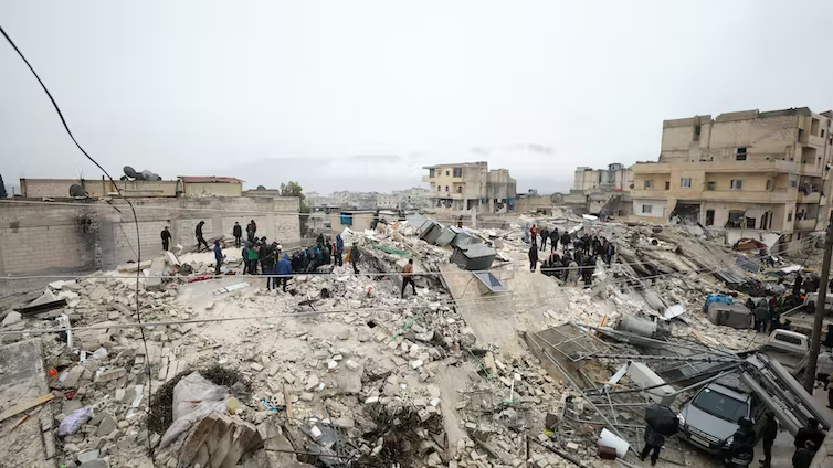 People standing around collapsed buildings that fell during the earthquake in Syria.